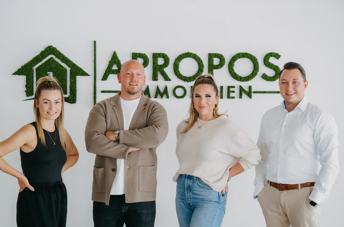 Das Team von APROPOS Immobilien vor dem Logo im Büro in Neukirchen-Vluyn